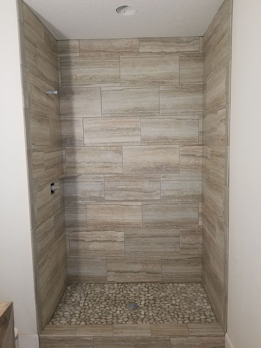 Shower stall with beige tile walls and pebble floor