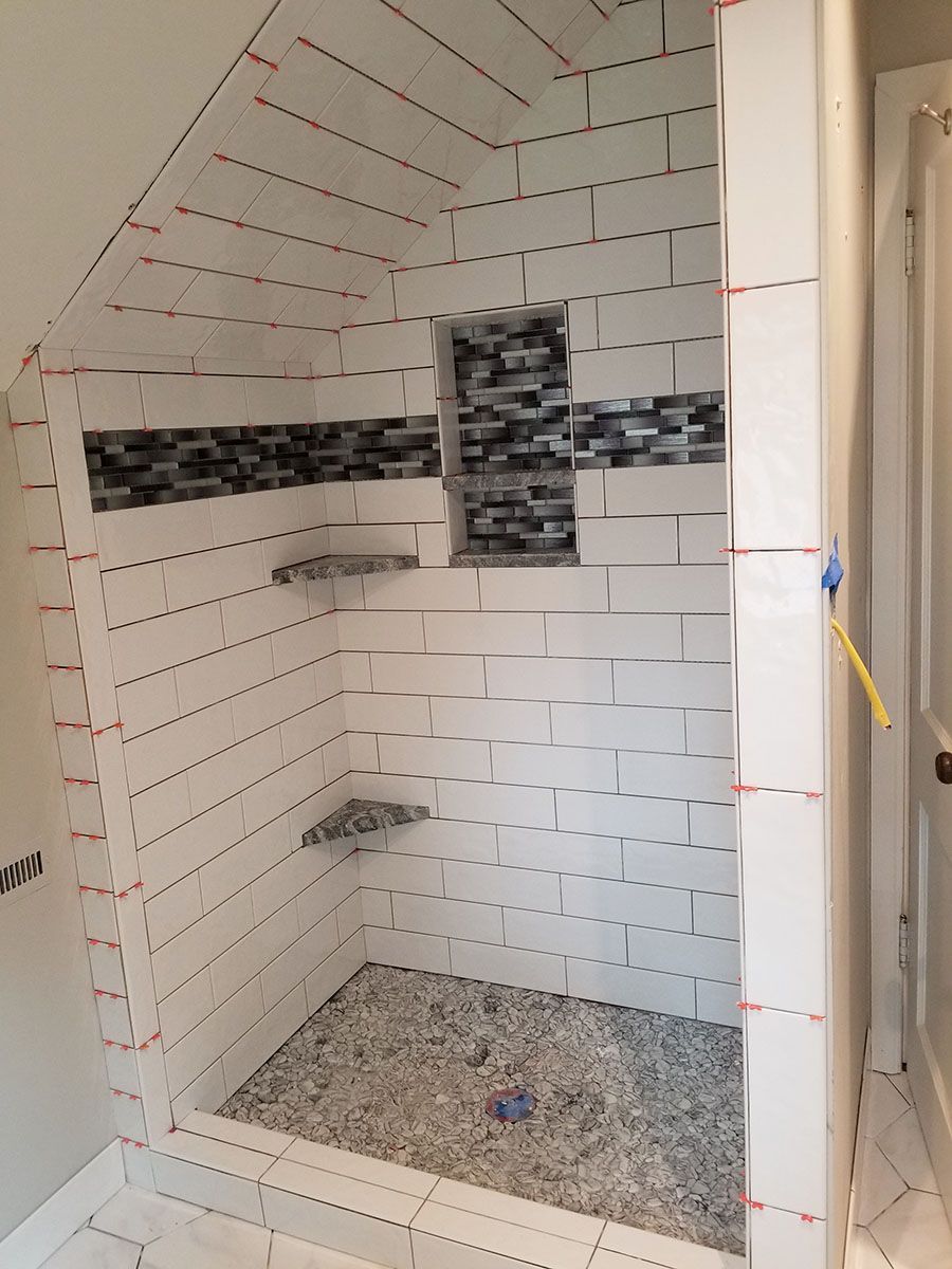 Shower under construction, white subway tiles with niche and pebble floor, red spacers
