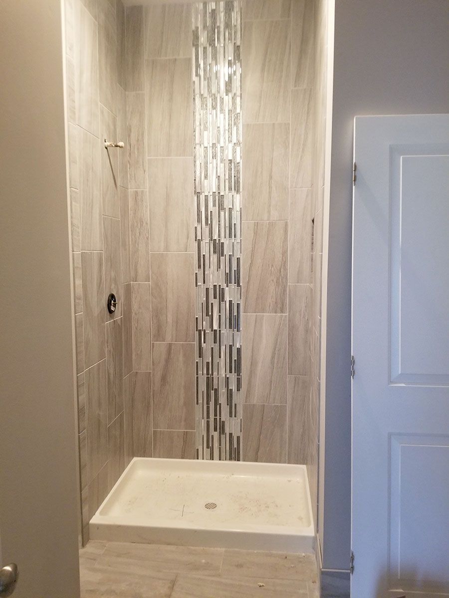 Shower stall with neutral-toned tiles and glass mosaic strip