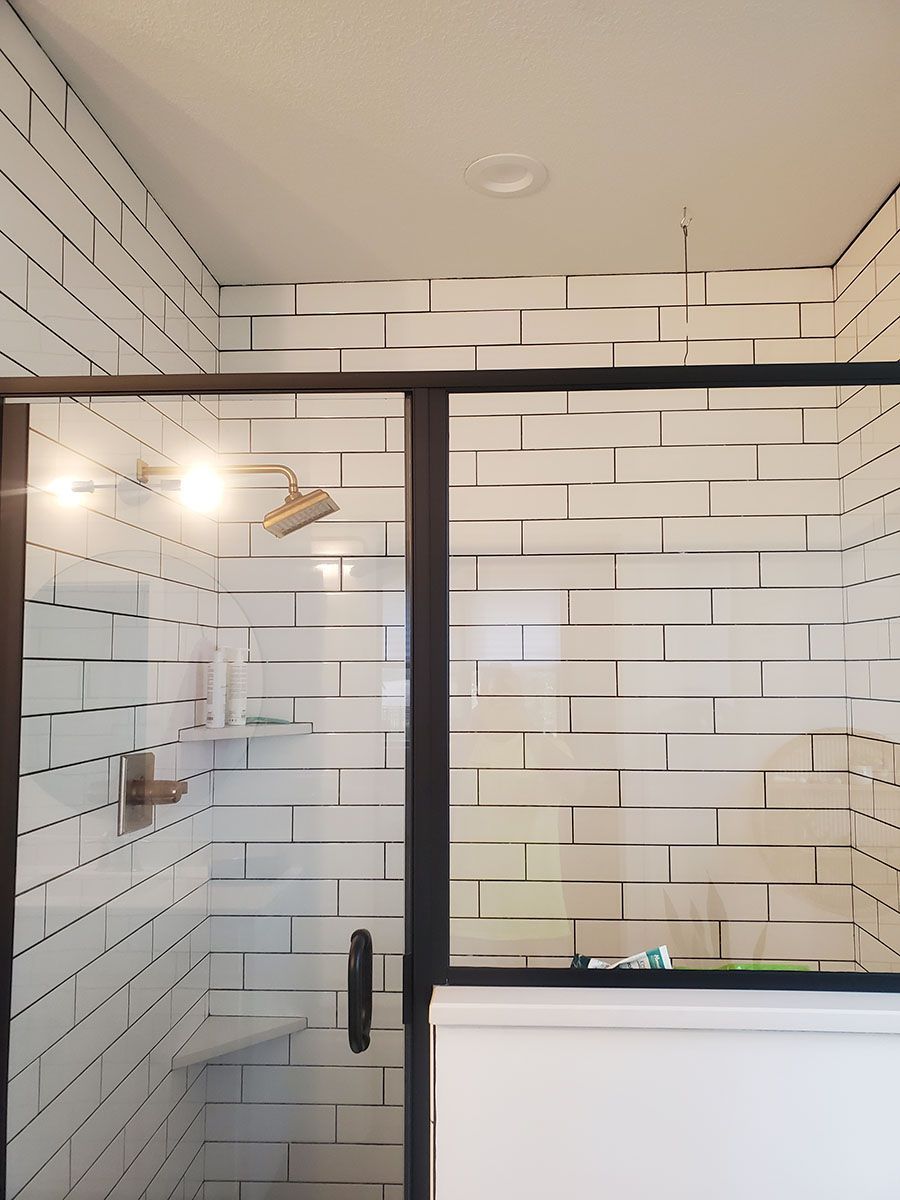 Shower with white brick-like tiles, a dark frame, and clear glass doors