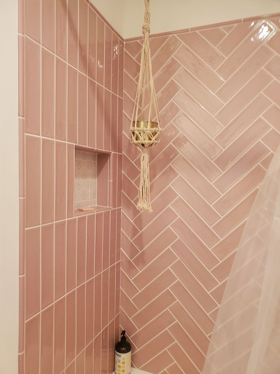 Pink tile shower with herringbone and vertical patterns; a hanging plant in a macrame holder