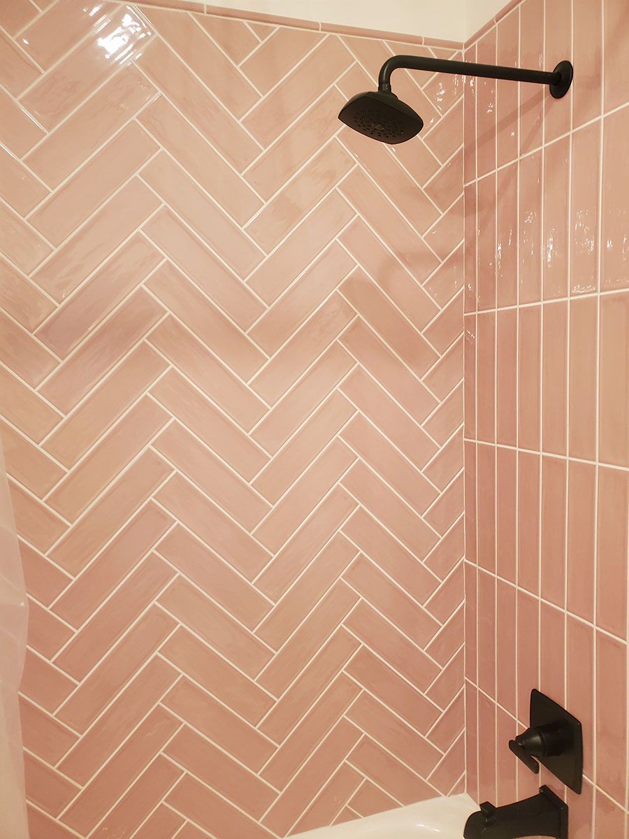 Pink tiled shower with black fixtures; herringbone pattern on one wall