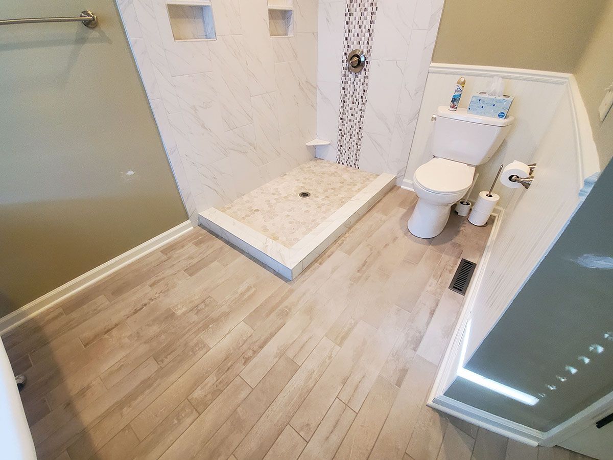 Bathroom with tiled shower, toilet, and light wood-look flooring
