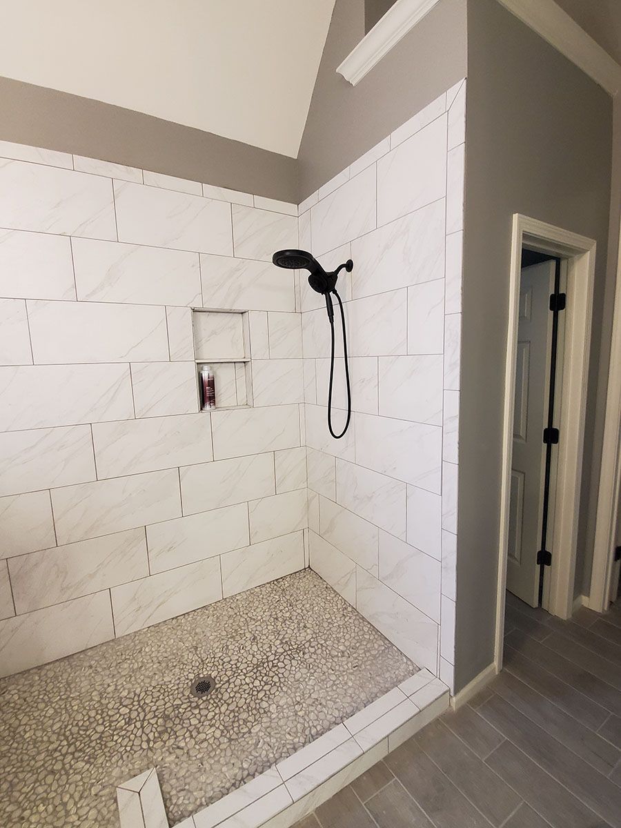 Tiled shower stall with pebble floor, black showerhead, and a recessed shelf