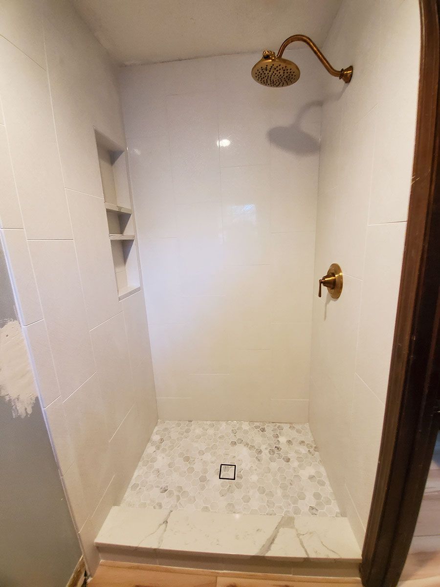 Newly renovated white tile shower with gold fixtures and marble floor