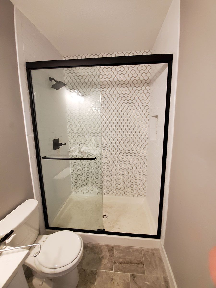 Black-framed shower with sliding glass door, black fixtures, and patterned tile in a small bathroom