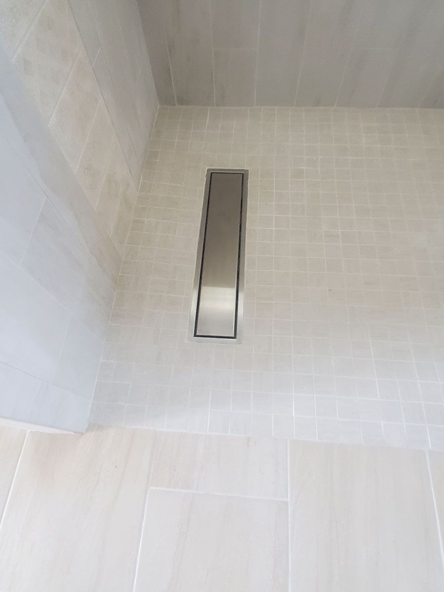 Silver linear shower drain set into tiled shower floor