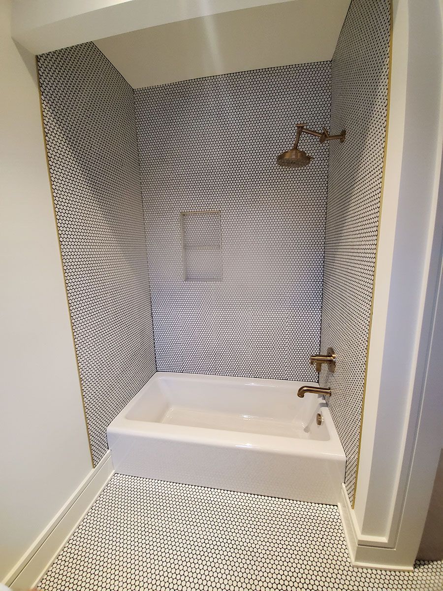 Bathroom with white tub, gold fixtures, and black and white patterned tile