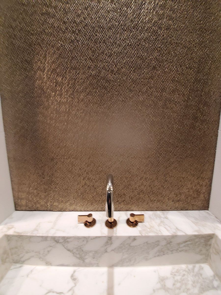 Marble sink with gold fixtures, against a textured brown wall