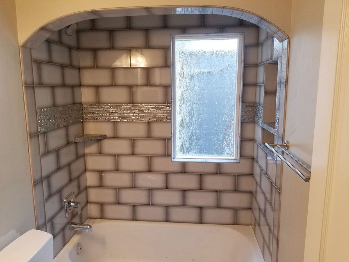 Bathroom with white and gray tiled walls, arched doorway, frosted window, and a bathtub