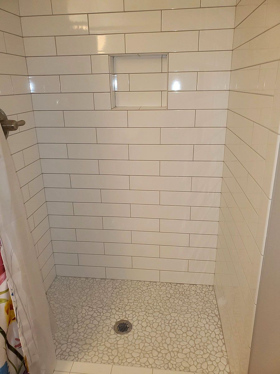 White tiled shower with pebble floor and built-in shelf