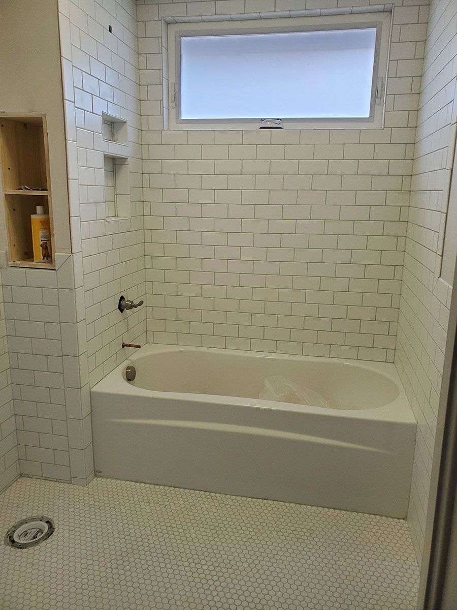 White tiled bathroom with a bathtub, showerhead, and a window
