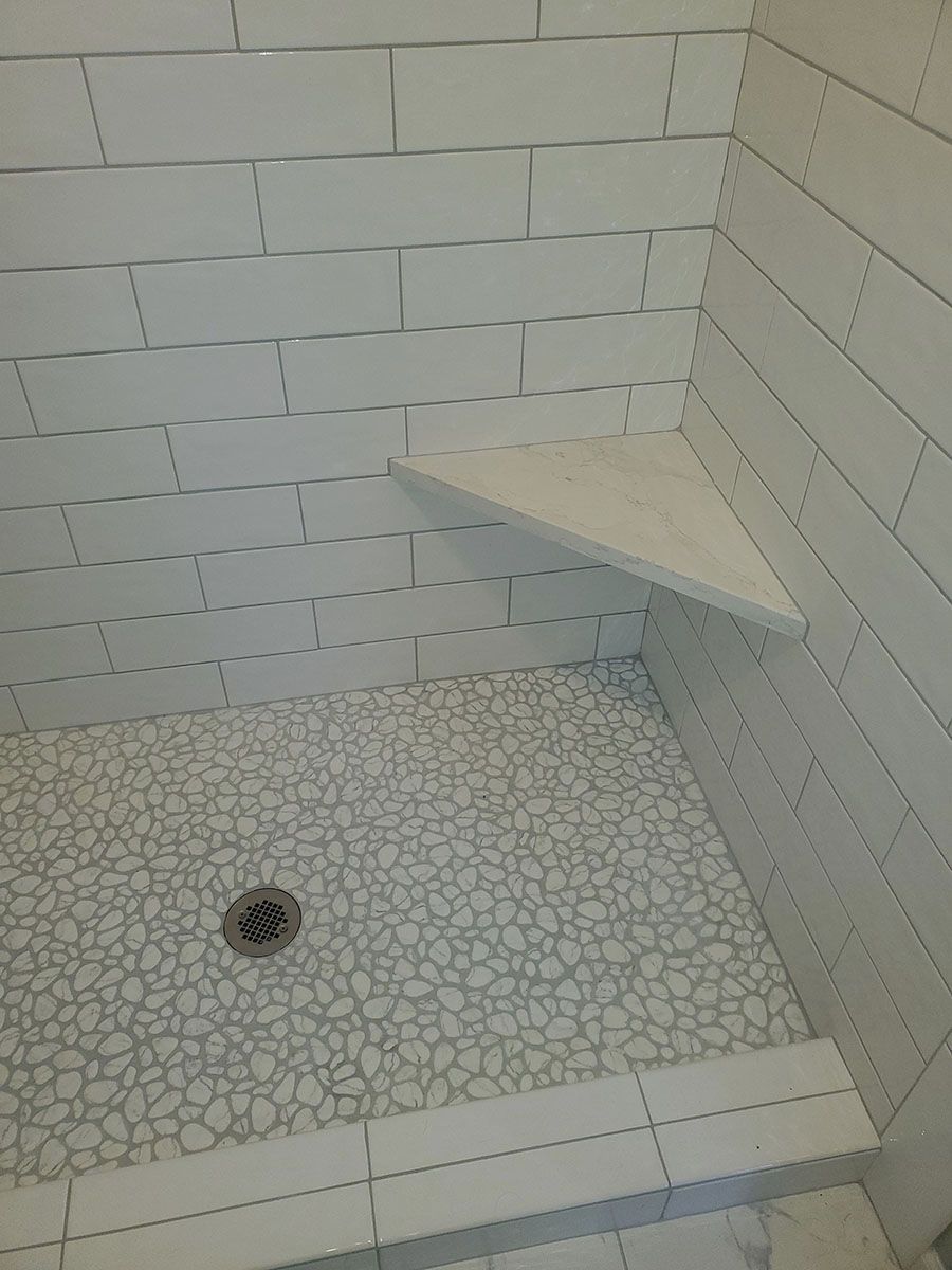 Shower interior with white tiled walls, pebble floor, and corner shelf