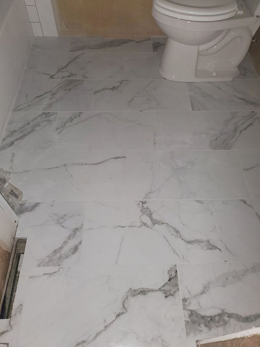 White marble-look bathroom tile floor installed, with a white toilet and light-colored walls
