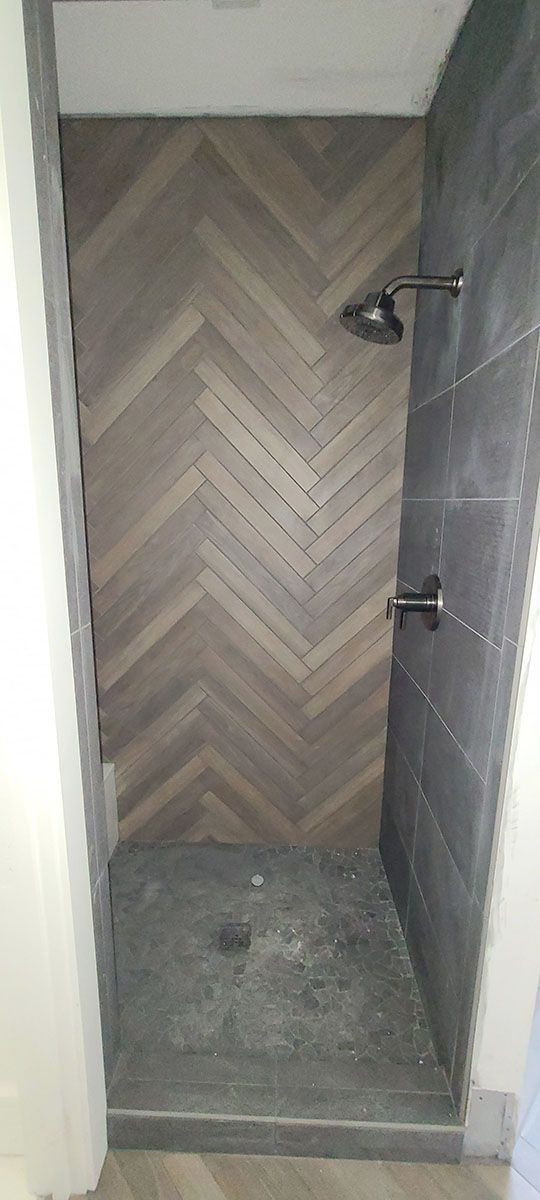 Shower stall with herringbone wood-look tile on the back wall and dark gray tile on the right