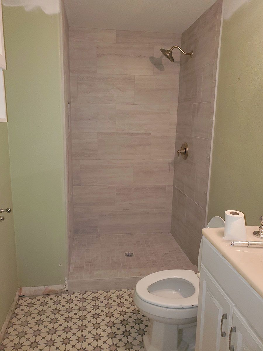 Bathroom with tiled shower, toilet, and vanity against green walls and patterned floor