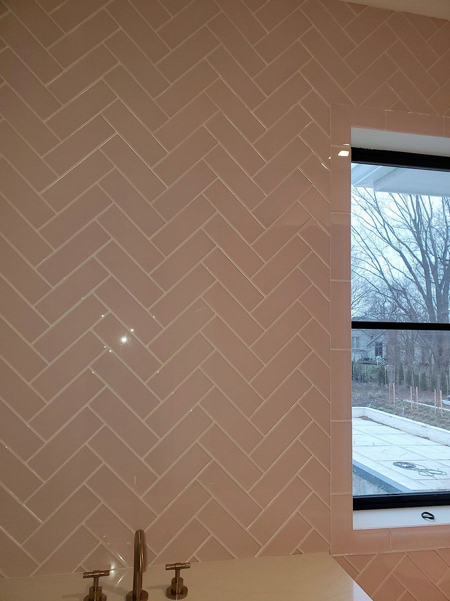Pink herringbone tile wall with a window; faucet visible