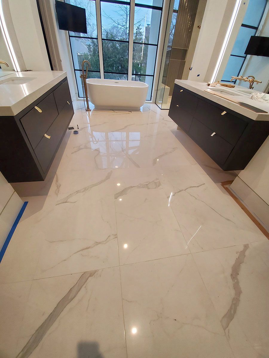 Luxurious bathroom with white marble floors, two dark wood vanities, and a freestanding tub