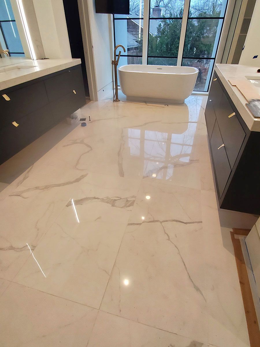 Luxurious bathroom with white marble tile floor, dark cabinets, and a freestanding tub in front of large windows