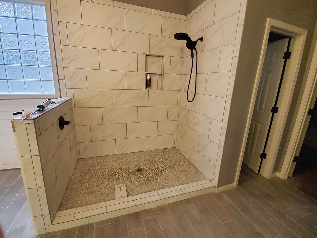 Newly tiled shower with pebble floor, black shower fixtures, and a tiled niche