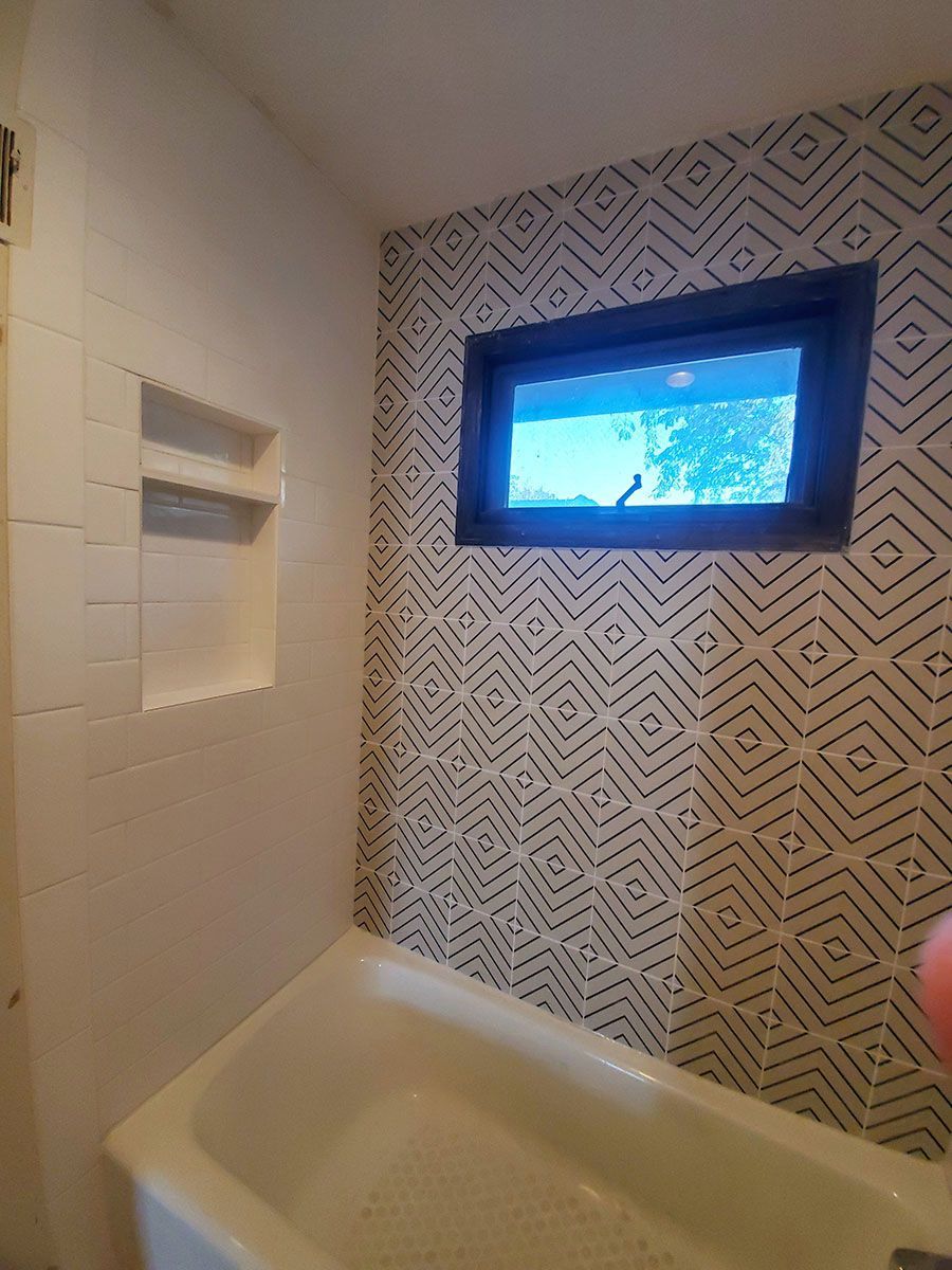 Bathroom with white tub, patterned tile wall, window with a view