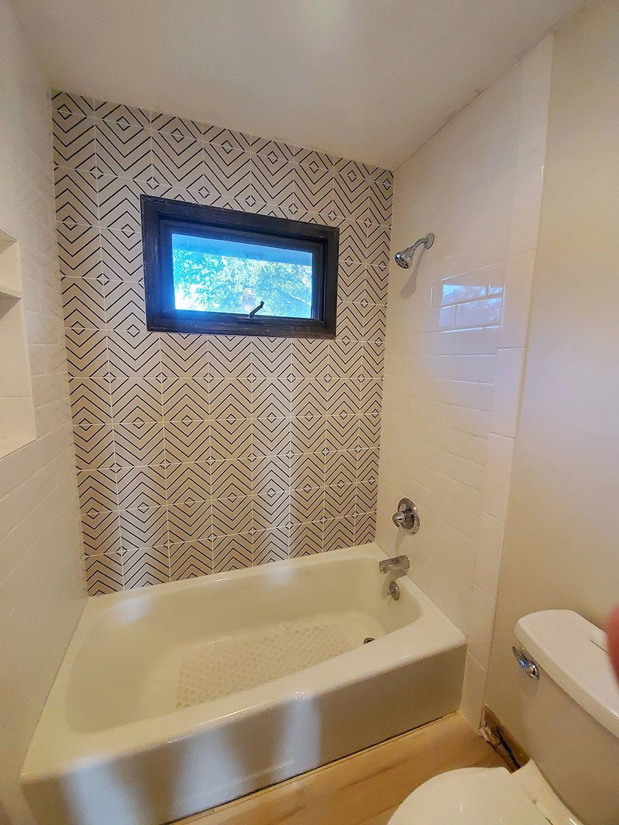 Bathroom with white tub, patterned wall tile, small window, and showerhead