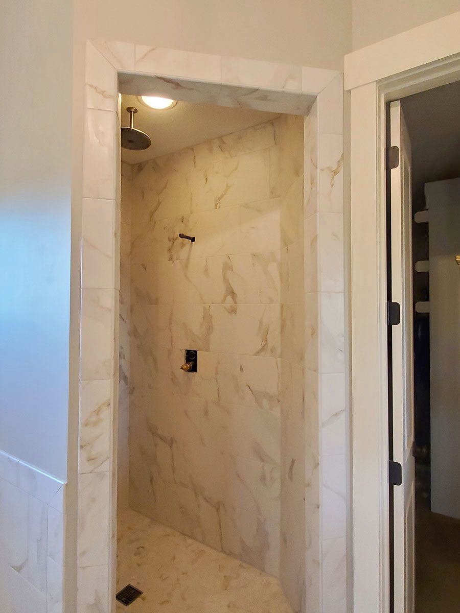 Marble-tiled walk-in shower with a framed doorway, shower head, and hardware; seen from outside the shower