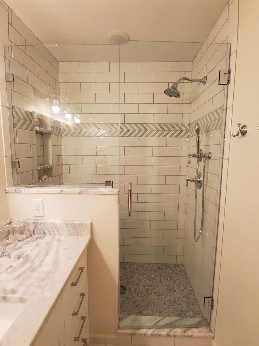 Modern shower with glass doors, white subway tiles, a gray accent, and a pebble stone floor