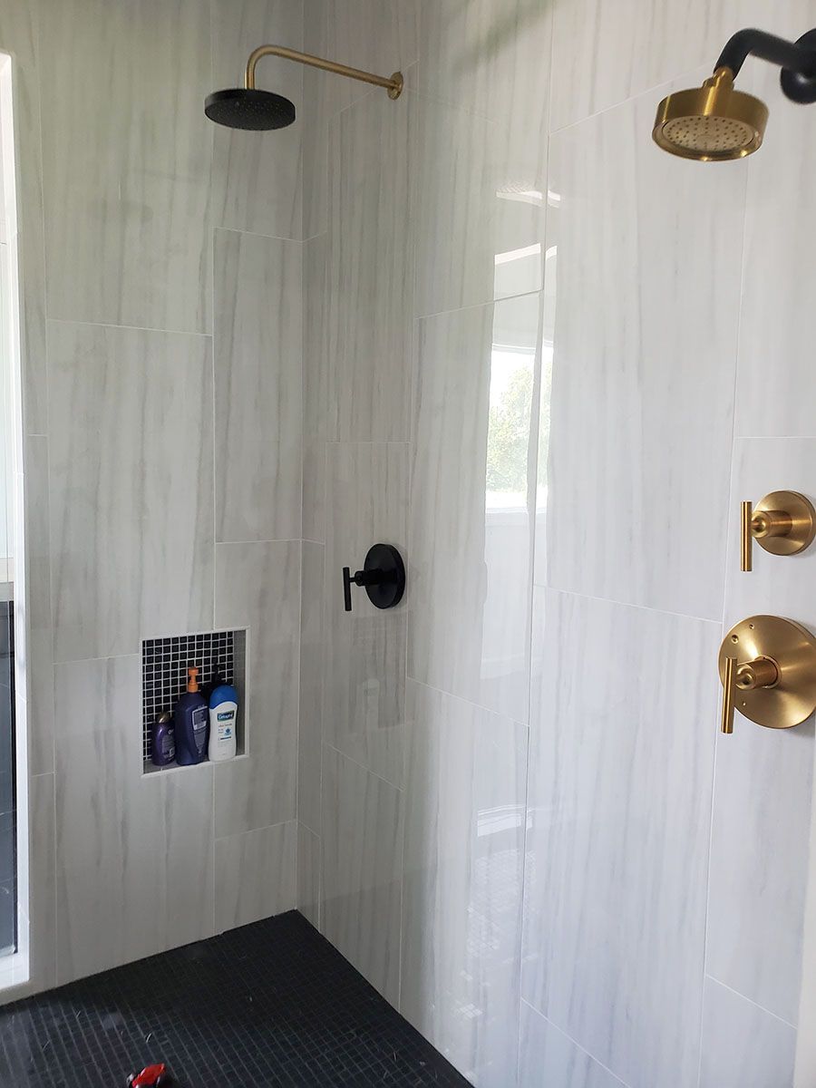 Bathroom shower with black and gold fixtures, white tiled walls, and a recessed shelf