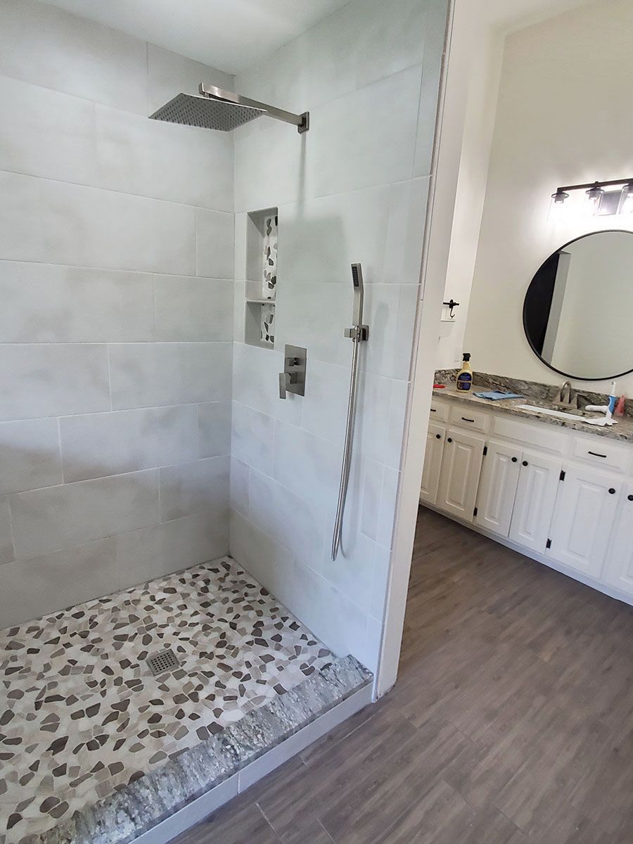 Modern bathroom with tiled shower stall, pebble floor, and white vanity