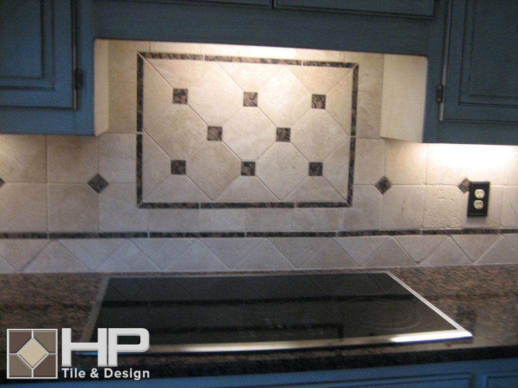 Kitchen backsplash with patterned beige tiles, dark square accents, and black cooktop.