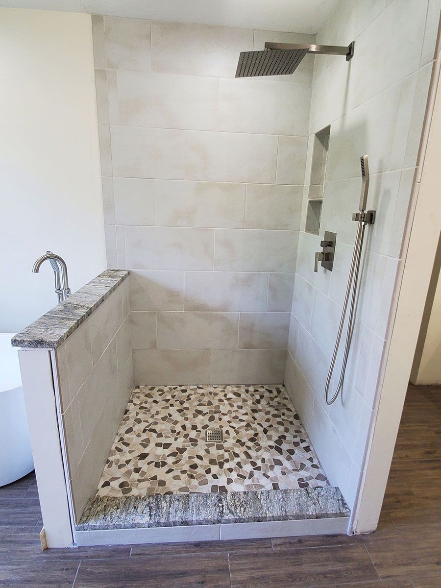 Newly tiled shower stall with pebble flooring, rain shower head, and recessed shelves