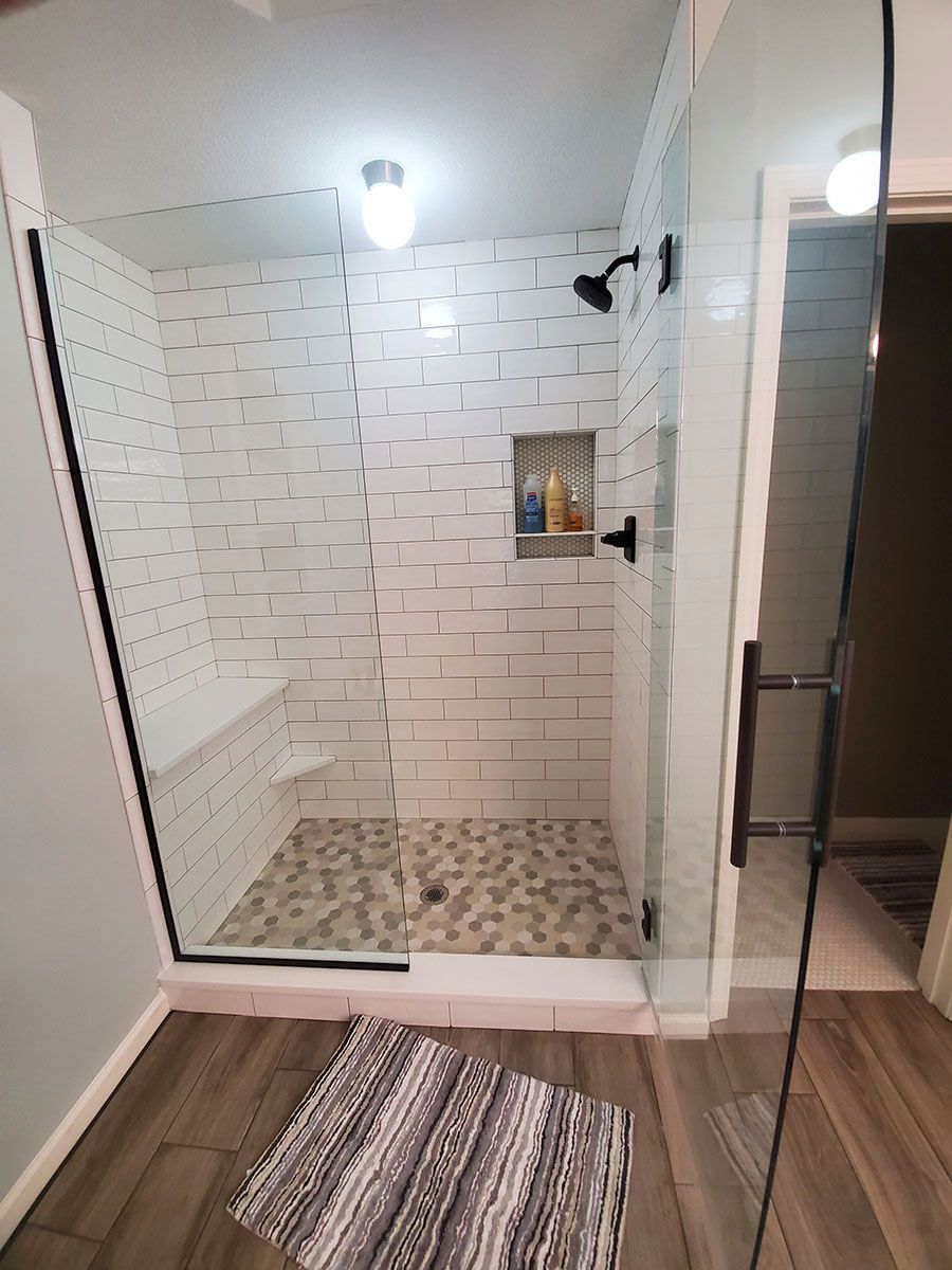 Modern shower with glass doors, white subway tile walls, pebble floor, and black fixtures