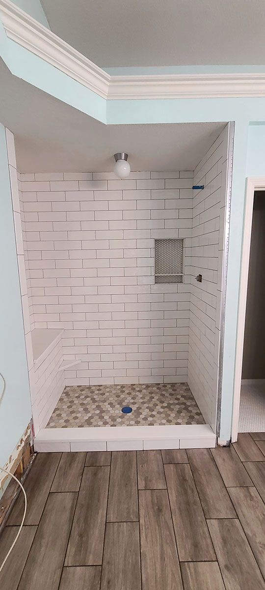 A newly tiled shower stall with a pebble stone floor, in a room with wood-look flooring