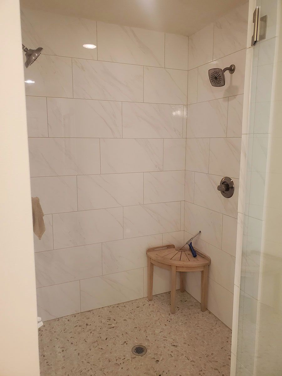 White-tiled shower with built-in bench, two showerheads, and a speckled floor