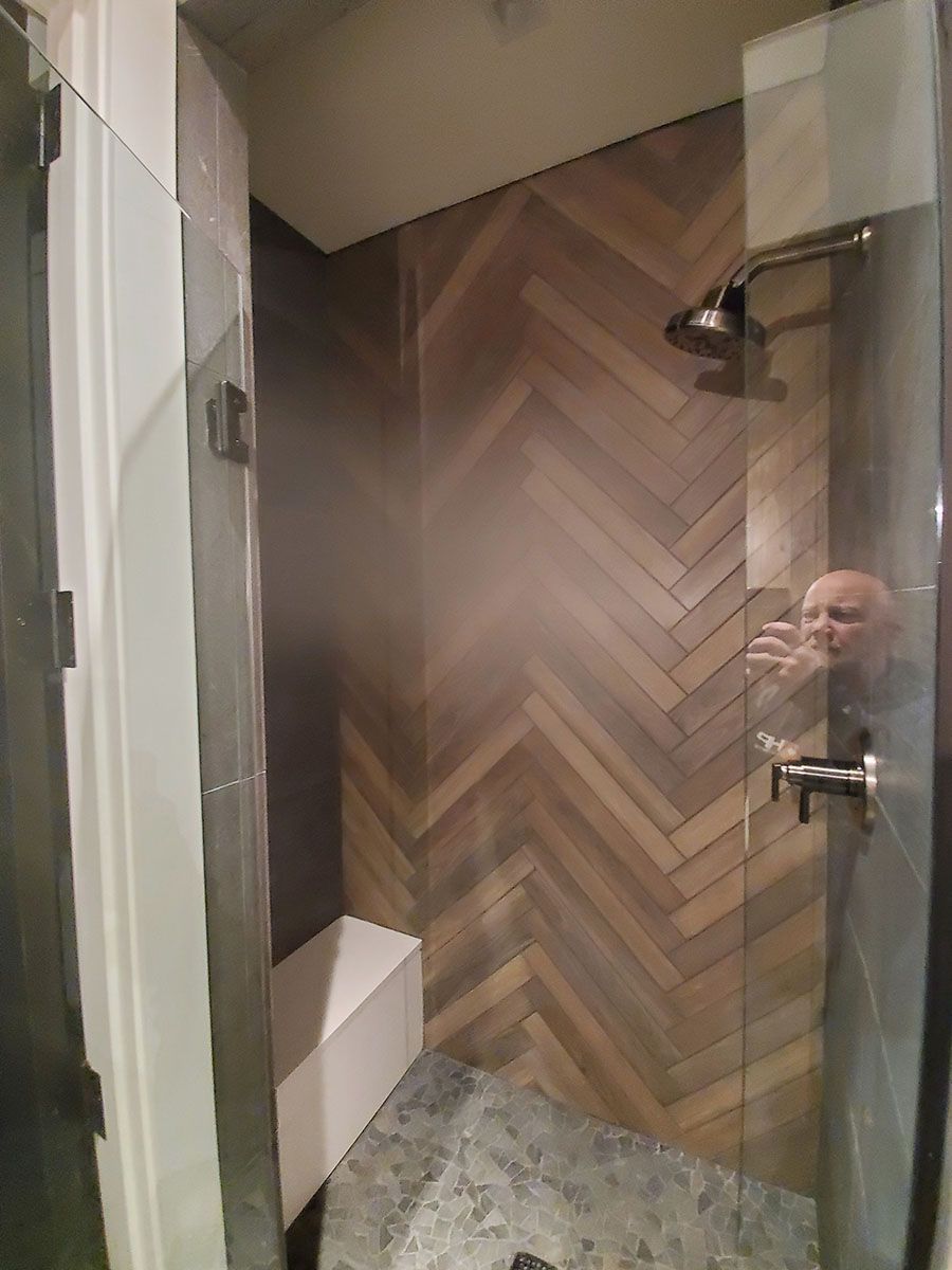Shower with wood-look herringbone tile, glass doors, and a chrome showerhead