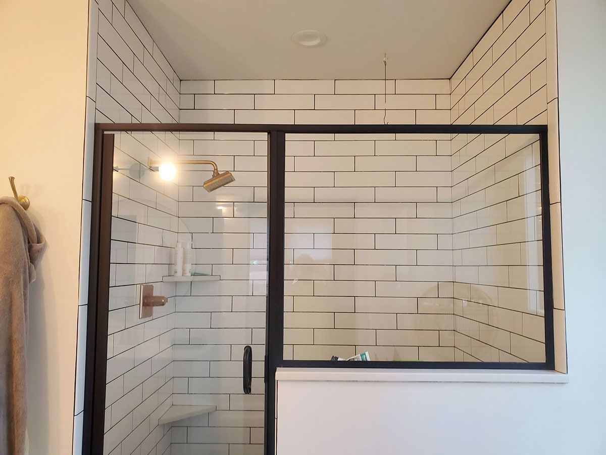 Shower stall with white brick-style tiles, black frame glass door, and a showerhead