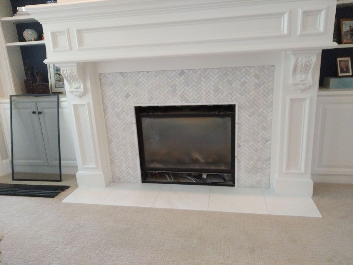 White fireplace with marble tile surround and black fireplace insert, in a room with light carpet