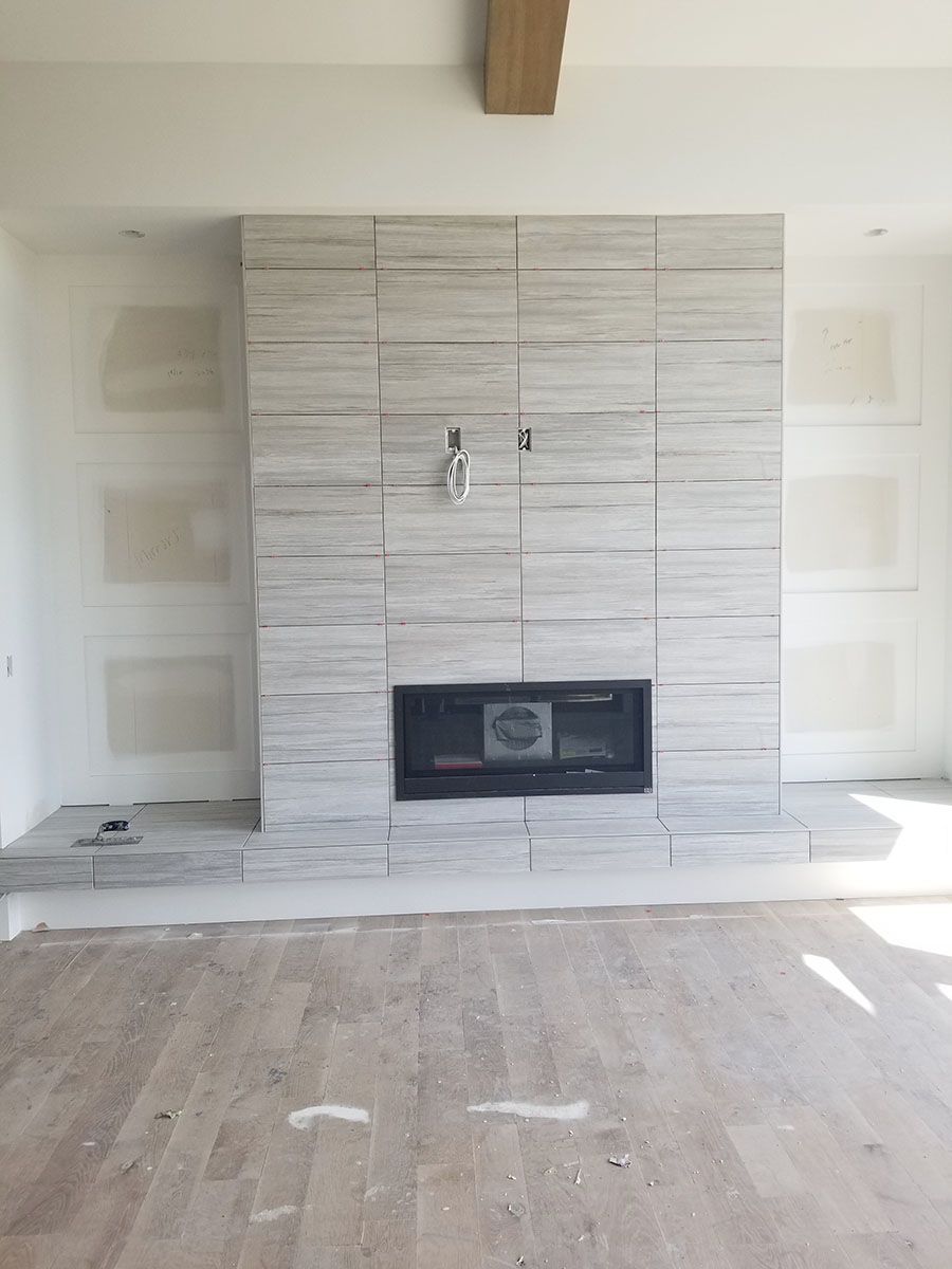 Fireplace under construction, covered in gray tile, with unfinished drywall and light wood flooring