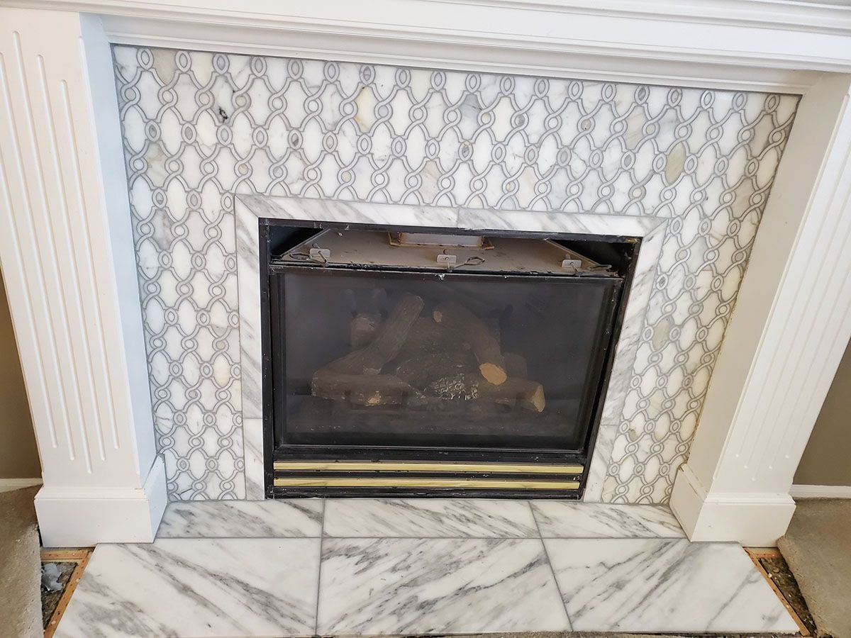 Fireplace with white marble tile surround and patterned accent, white mantel, and black firebox
