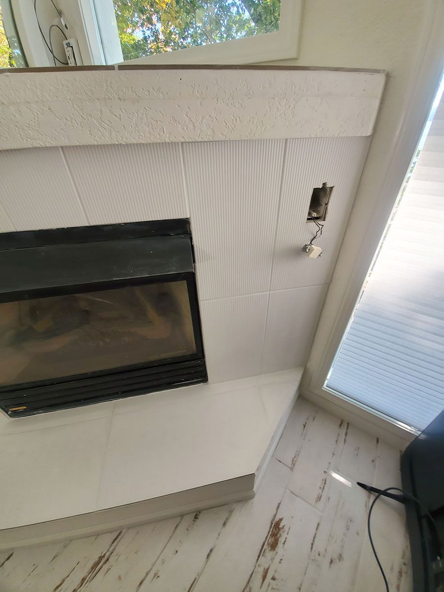 White tiled fireplace with a black insert, near a window with blinds