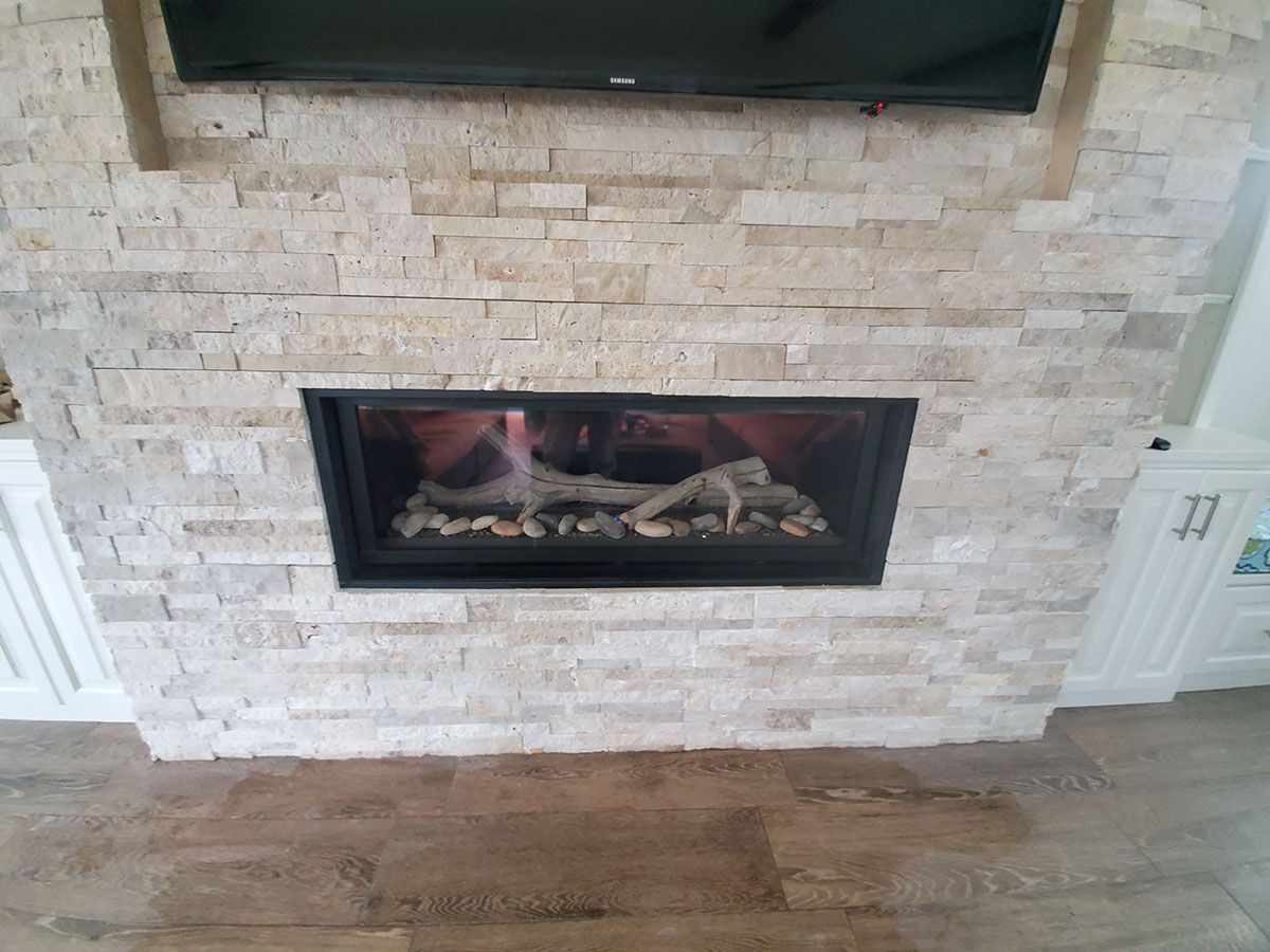 Fireplace with light stone facade, black trim, and a lit fire with decorative logs, beneath a mounted TV