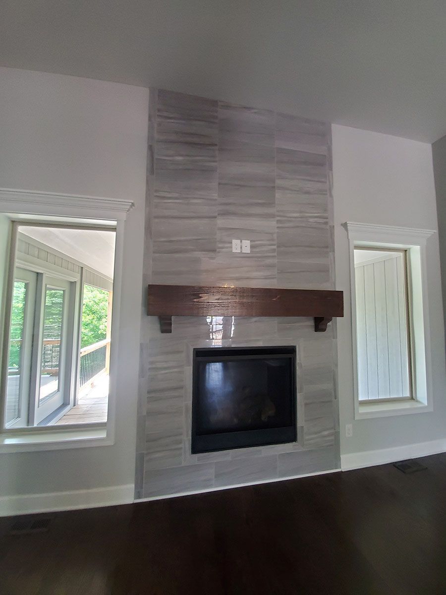 Fireplace with gray tiled surround, dark wood mantel, and black firebox, flanked by windows