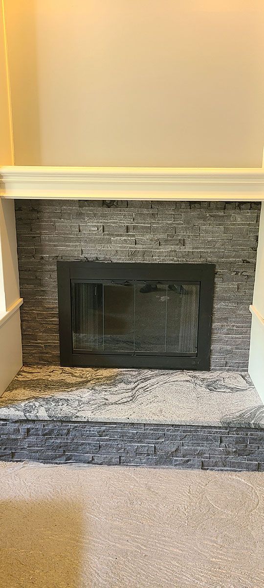 Fireplace with stone facade, dark framed glass door, and a white mantel in a light-colored room
