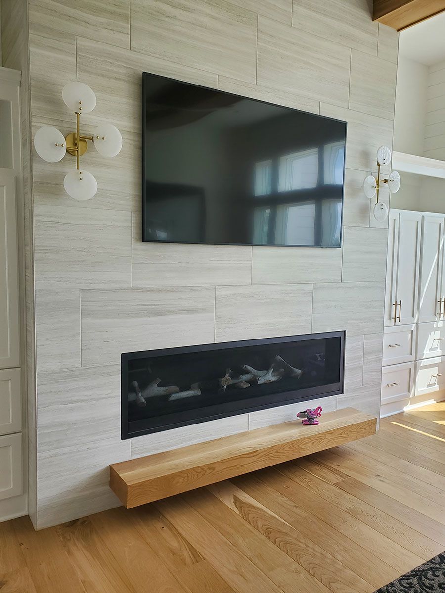 A modern fireplace with a large TV mounted above, flanked by sconces. Wooden floor and floating shelf