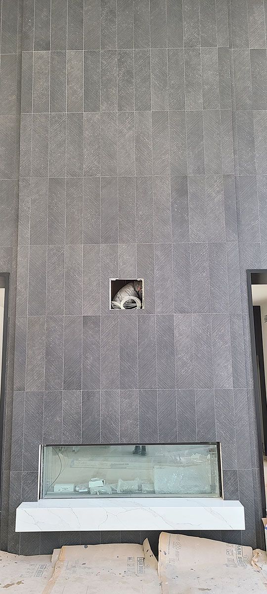 Gray tiled wall with a window-like structure. There is a square cut-out with piping above the structure