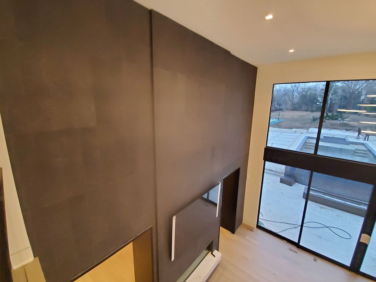 Dark brown paneling covers a wall with a fireplace opening and tall windows overlooking a backyard and pool