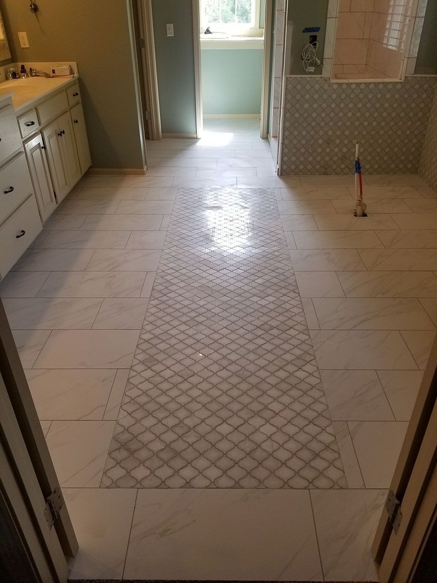 Bathroom floor with patterned tile inlay, light-colored walls and vanity, natural light from the window