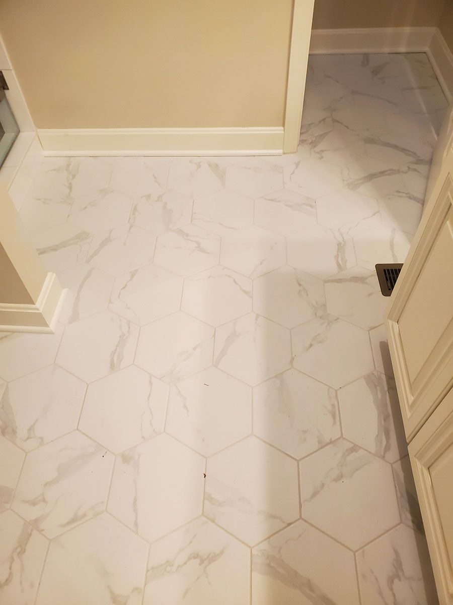 White marble-patterned hexagon tile bathroom floor; adjacent white trim, cabinet