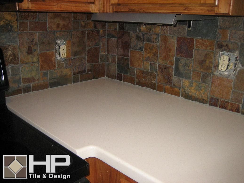 Kitchen with cream-colored countertop, multi-colored tile backsplash, wooden cabinets, and electrical outlets.